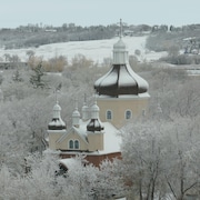 Une église orthodoxe saupoudrée de neige se trouvant parmi des arbres dégarnis  