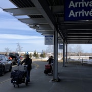 Des voyageurs poussent des bagages à la sortie de l'aéroport.