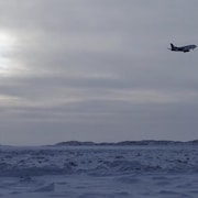 Un avion prend son envol au-dessus d'un champ enneigé.
