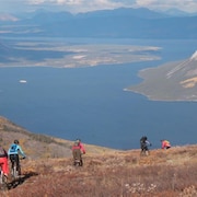 Des amateurs de vélo de montagne suivent une piste au sommet d'une montagne avec un grand lac en arrière-plan.