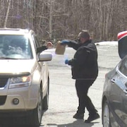 Un homme tend un sac de papier brun à une personne qui sort le bras de la fenêtre de son automobile.