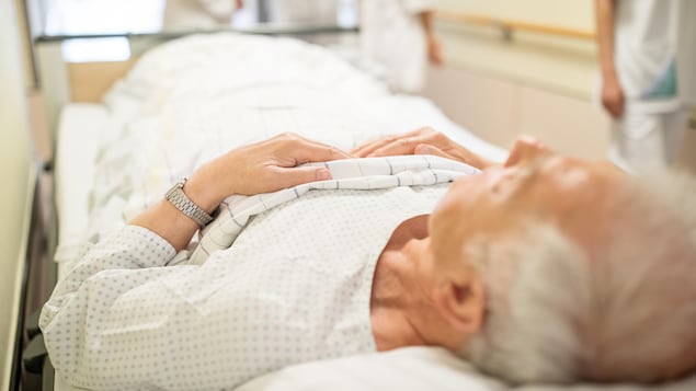 Un homme âgé est allongé dans un couloir d'hôpital.