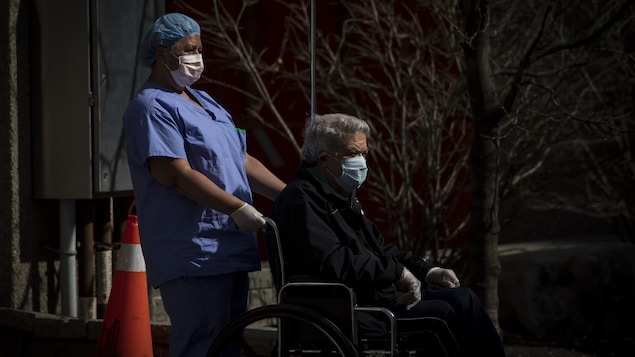 Une femme portant un masque de protection pousse le fauteuil roulant d'un homme portant lui aussi un masque.