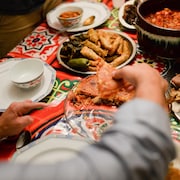 Une main d'homme se sert de la nourriture parmi plusieurs plats disposés sur une table colorée.