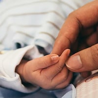Une main de femme tient les doigts d'un bébé.