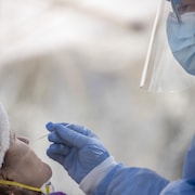 Une infirmière portant une visière insère une tige dans le nez d'une patiente lors d'un test de dépistage.