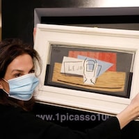 Une femme portant un masque hygiénique tient la toile de Picasso entre ses mains.