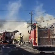 Des camion de pompiers devant un épais panache de fumée.