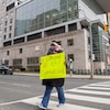 Une femme masquée tient une pancarte devant elle en traversant une rue près d'un hôpital. 