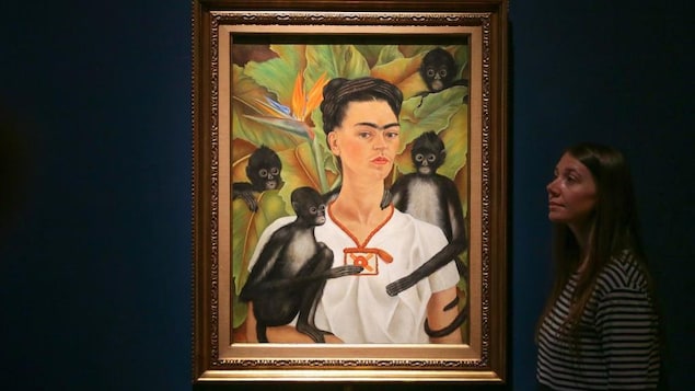 Le tableau, exposé sur un fond bleu, représente Frida Kahlo entourée de 4 petits singes noirs.