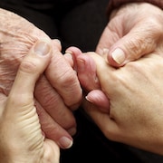 Gros plan sur une personne âgée qui tient les mains d'une personne plus jeune.
