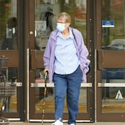 Une personne avec une canne qui porte un masque devant les portes d'un commerce.
