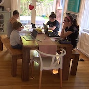 Une mère et ses trois enfants sont assis à la table de la cuisine. Ils suivent tous des cours à distance.