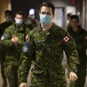 Des militaires des forces armées canadiennes, la plupart portant un masque, dans un couloir d'un collège.
