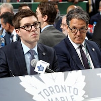 Deux hommes en complet sont assis à une table lors du repêchage annuel de la Ligue nationale de hockey.