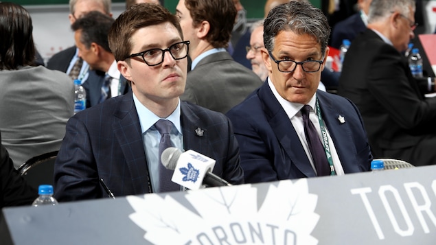 Deux hommes en complet sont assis à une table lors du repêchage annuel de la Ligue nationale de hockey.