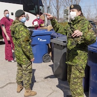 Plan large de militaires portant des masques devant des bacs de recyclage.