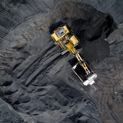 Une pelle mécanique déverse du charbon dans une benne, dans une mine à ciel ouvert, le tout vu du ciel.