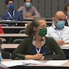 Des gens portant des masques écoutent dans une salle de classe.