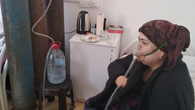 Une femme assise sur un lit porte un masque à oxygène.