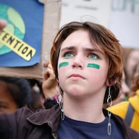 Gros plan du visage d'une jeune manifestante qui regarde en l'air, le poing brandi, à l'extérieur.