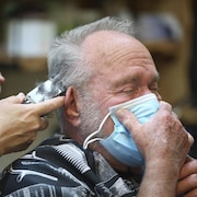 Un homme se fait couper les cheveux en tenant un masque sur son visage.