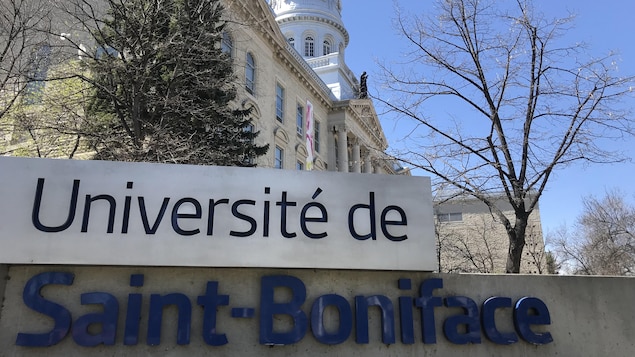 Une affiche où il est écrit : Université de Saint-Boniface avec en arrière-plan l'édifice qui abrite l'Université.