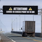 Un camion lourd passe sous le tableau numérique du pont, qui annonce un point de contrôle de la COVID-19 dans 14 kilomètres.