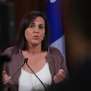 Une femme parle dans un micro devant un drapeau du Québec.
