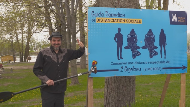 Il tient son micro devant une pancarte qui explique les règles de la distanciation sociale.