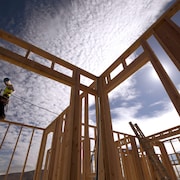 Un travailleur debout sur la structure d'une maison en construction.