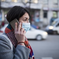 Une femme portant un masque marche dans la rue en parlant au téléphone.