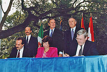 Photographie des premiers ministres du Canada, des États-Unis et du Mexique debout derrière les trois ministres du Commerce international de ces pays, signant l'Accord de libre-échange nord-américain.