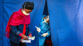 a healthcare worker speaks to a colleague through a small tent opening