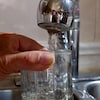 Un homme remplit un verre d'eau sous un robinet.