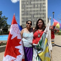Kerry Bellegarde Opoonechaw et Star Andreas posent devant l'hôtel de ville de Regina en tenant des drapeaux du Canada et du traité numéro 4.