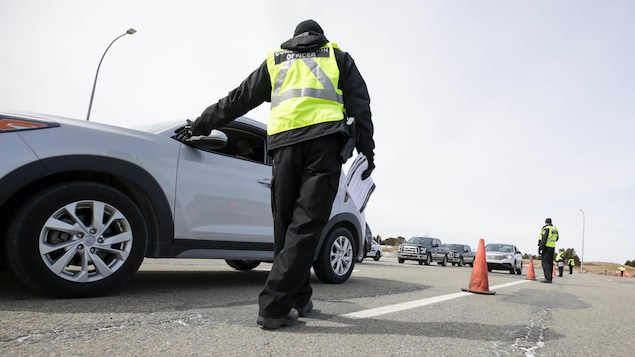 Un agent vêtu d'une veste jaune et avec des documents à la main s'approche d'une automobile.