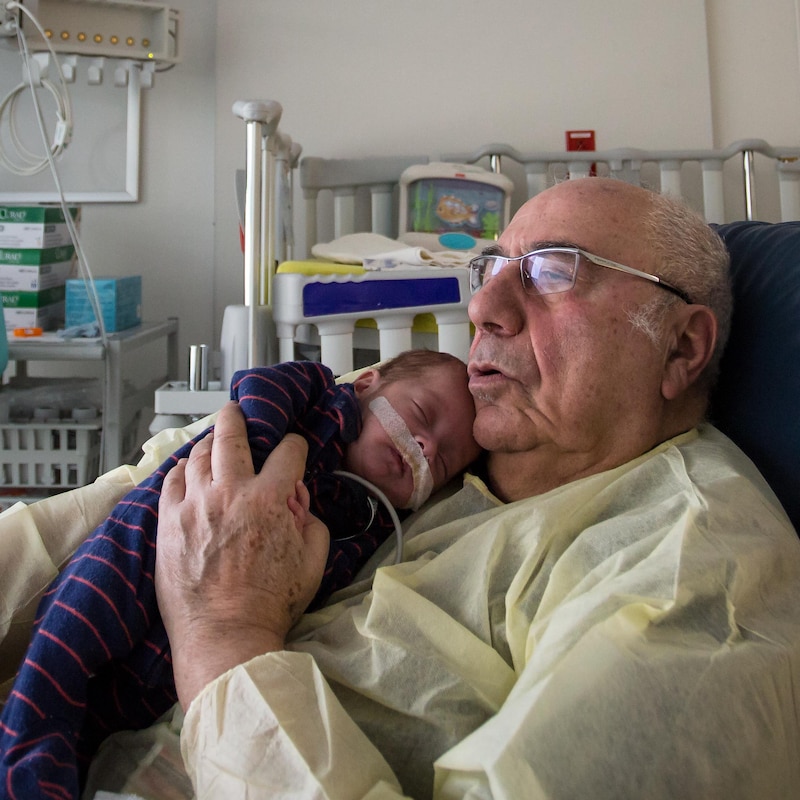 Un bébé dort dans les bras d'un homme âgé.