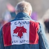 Sur le manteau de l'homme se trouve un drapeau du Canada à l'envers sur lequel on peut lire « Pas de Canada sans Premières Nations ». 
