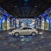 Une voiture au milieu d'un hangar désert. Des œuvres de Van Gogh sont projetées sur le sol et sur les murs.