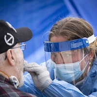 Une professionnelle de la santé effectue un test de dépistage de la COVID-19 sur un homme âgé.