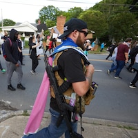 Un homme armé d'un fusil se promène en périphérie d'une manifestation antiraciste.