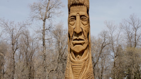 Cameron Adams a côté d'une grande statue de bois à l'effigie d'un chef autochtone. 