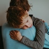 Une personne porte dans ses bras un enfant qui a de la peine.