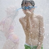 Un garçon portant des lunettes de piscine se fait arroser par un jet d'eau.