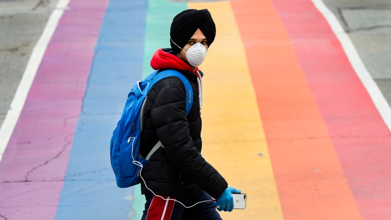 A man wearing a mask crosses the street during the COVID-19 pandemic in Toronto on Tuesday, April 28, 2020. THE CANADIAN PRESS/Nathan Denette