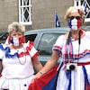 Deux femmes costumées portent des masques non médicaux aux couleurs du drapeau de l'Acadie.