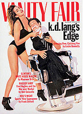 Cover of Vanity Fair magazine from August 1993 showing k.d. lang reclining in a barber chair with eyes closed and holding a compact mirror. She has shaving foam on her chin and is wearing an open-collar white shirt, black and white striped tie, dark color pinstripe vest and cuffed pants, and black lace boots. Supermodel Cindy Crawford is holding a straight razor to lang's chin while lang's head rests on her breast. Crawford is wearing a one-piece black bathing suit and high heel black boots, with head thrown back as her long hair cascades down her back.