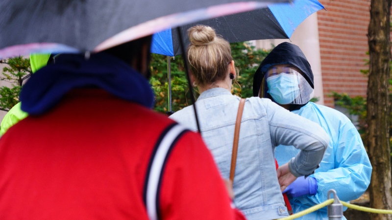 A health-care worker hands out masks to people waiting in line in the pouring rain outside a walk-in COVID-19 test clinic in Montreal, on Wednesday, October 7, 2020. THE CANADIAN PRESS/Paul Chiasson