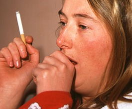 Woman coughs while smoking a cigarette - Copyright: Science Photo Library